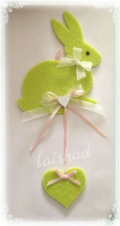 a green felt bunny with a bow and heart hanging from it's back on a white background