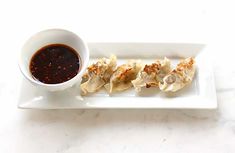 a white plate topped with dumplings next to a cup of sauce