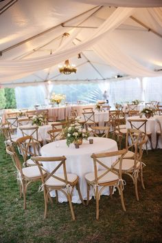 an outdoor tent with tables and chairs set up for a wedding reception in the grass