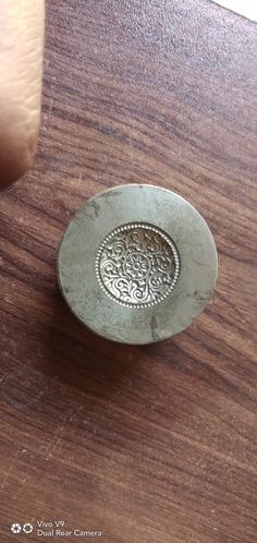 a small metal object sitting on top of a wooden table next to a person's finger