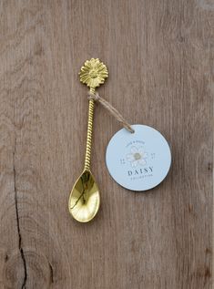 a gold spoon with a tag attached to it sitting on a wooden surface next to a stick