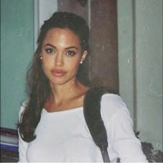 a woman in white shirt and backpack standing next to door with handbag on shoulder