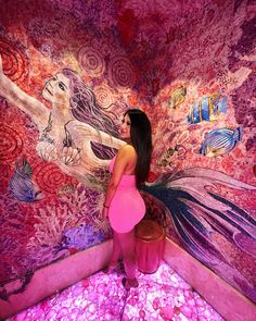 a woman is standing in front of a wall with flowers and mermaids on it