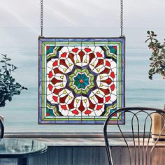 a stained glass window hanging over a table next to a chair and potted plant