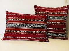 two red pillows sitting on top of a bed next to each other in front of a white wall