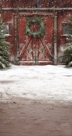 a red barn with a wreath on the door and snow covered trees in front of it