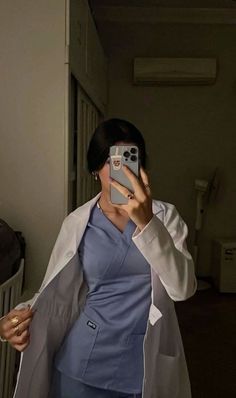 a woman in scrubs taking a selfie with her cell phone while wearing a white lab coat