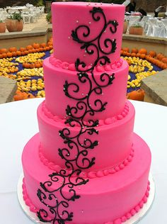 a three tiered pink cake with black swirls on the top and bottom layer