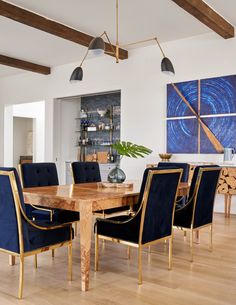 a dining room table with blue chairs and artwork on the wall in the back ground