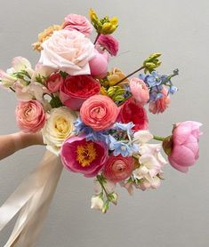 a bouquet of flowers is being held up by someone's hand in front of a gray wall