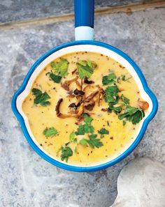 a blue and white bowl filled with soup on top of a gray counter next to a spoon