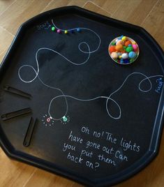 a black tray with chalk writing on it and a bowl of candy in the middle