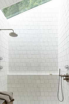 a white tiled bathroom with a skylight above the bathtub, shower head and handset