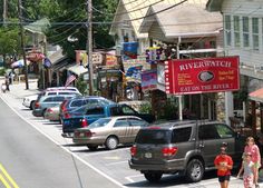 several cars parked on the side of a street next to shops and businesses with people walking by