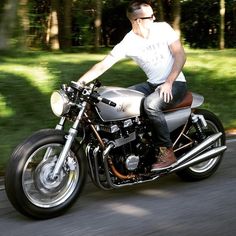 a man riding on the back of a silver motorcycle down a curvy road