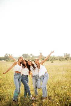 three girls are standing in the middle of a field with their arms up and smiling