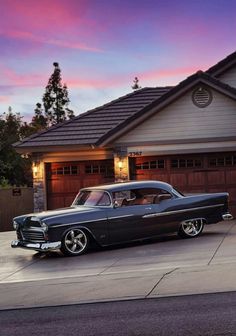 an old car is parked in front of a house at dusk with the sun going down