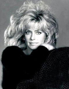 a black and white photo of a woman with blonde hair posing for the camera, her hand on her shoulder