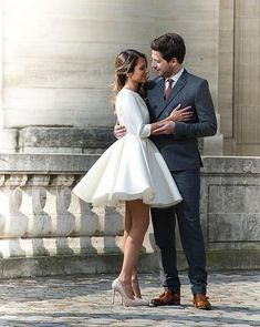 a man and woman standing next to each other in front of a stone building with columns