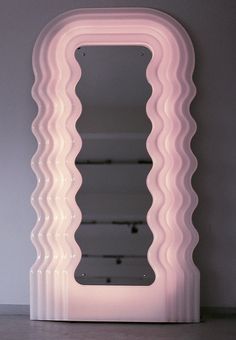 a large pink mirror sitting on top of a table next to a wall mounted shelf