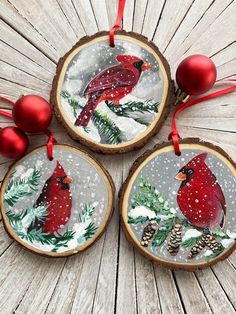 three christmas ornaments with red cardinals and pine cones hanging from them on wood planks