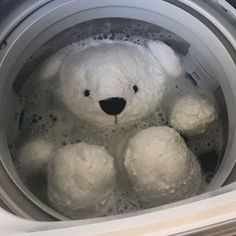 a white teddy bear sitting in a washing machine filled with foamy bubbles and water