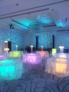 a room filled with lots of tables and chairs covered in white tablecloths under colorful lights