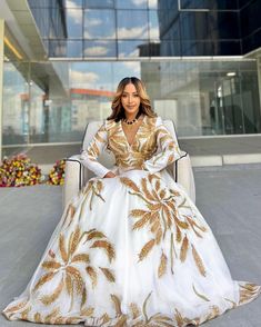 a woman sitting in a chair wearing a white and gold dress with palm leaves on it