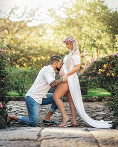 a man kneeling down next to a woman in a white dress and floral headband