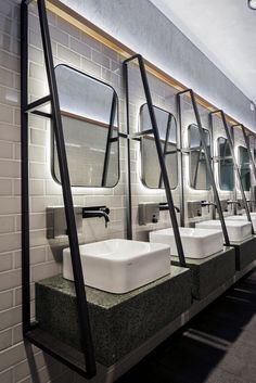 a row of white sinks sitting next to each other in a public restroom with mirrors on the wall