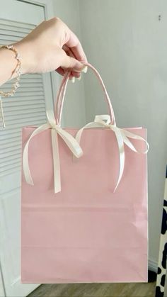 a person holding a pink shopping bag with white ribbon on the front and bottom handles