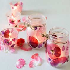 pink and red flowers are in glass jars with lights on the table next to them