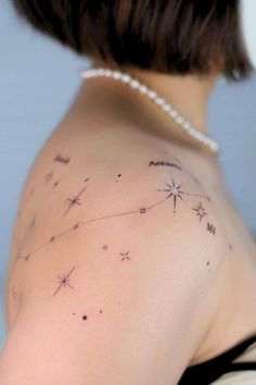 the back of a woman's shoulder with tattoos on her left arm and stars in the sky