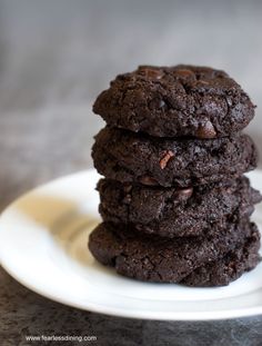 three chocolate cookies stacked on top of each other in a white plate next to a glass of milk