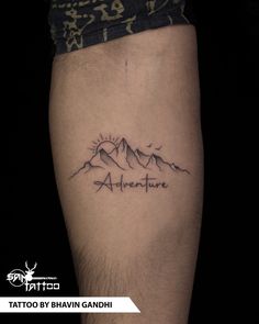 a tattoo with the words adventure written on it and mountains in the distance behind it