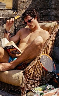 a shirtless man sitting in a wicker chair holding a tennis racquet