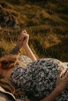 a woman laying in the grass holding her hand up