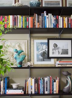 a bookshelf filled with lots of books next to a vase and framed pictures