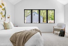 a bedroom with white walls and carpeted flooring has three windows that look out onto the backyard