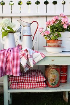 a table with flowers and watering can on it next to a white picket board fence