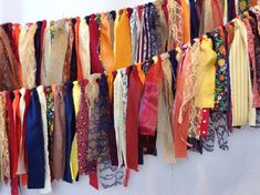 an assortment of scarves hanging on a wall with ribbons attached to the side of them