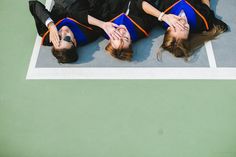 three people in graduation gowns laying on the ground with their arms around each other