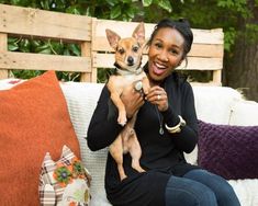 a woman sitting on a couch holding a small dog in her lap and smiling at the camera