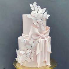 a three tiered wedding cake with white butterflies on the top and pink ribbon around it