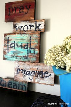 three wooden signs that say work laugh imagine dream and pray on a table next to a blue vase with white flowers