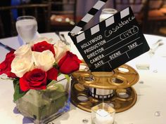 red and white roses are in a vase next to a movie clapper on a table