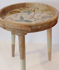 a small wooden table with birds painted on the top and bottom, sitting on a white surface