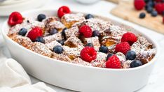 a white dish filled with french toast and berries