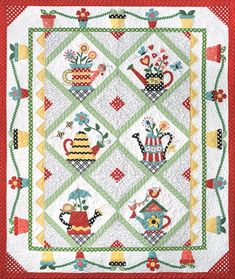 a quilted table topper with teapots and flowers on the front, in red