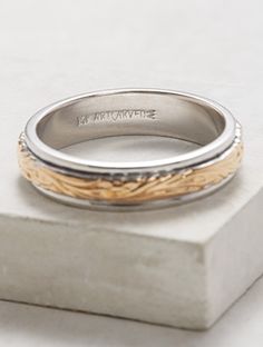 a silver and gold wedding ring sitting on top of a stone block